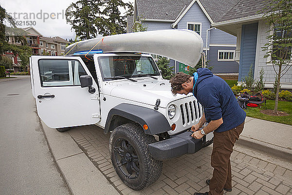 Ein Abenteurer bindet sein Kanu auf dem Dach seines Jeeps in einer Vorstadtumgebung fest