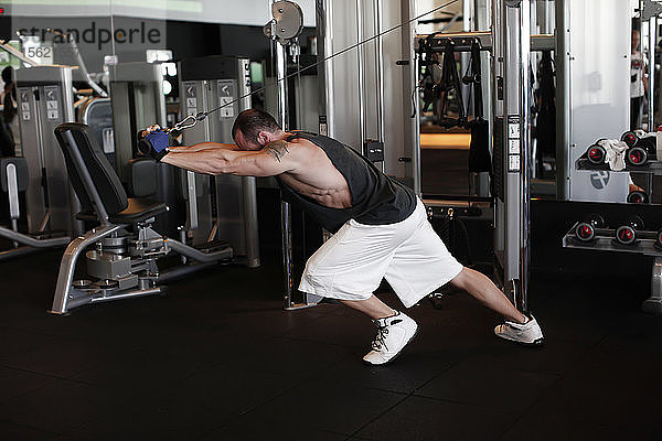 Porträt eines muskulösen Mannes  der an einem speziellen Sportgerät im Fitnessstudio trainiert