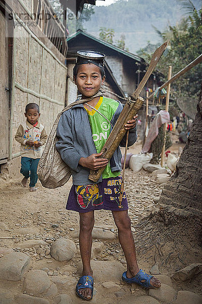 Ein Junge posiert stolz mit seiner Tauchermaske  seinem Speergewehr und seinem selbstgebauten Saiteninstrument in Ban Huay Phouk  Laos.