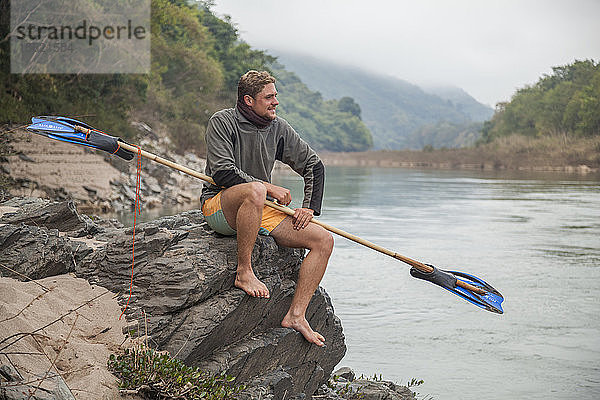 Jan aus den Niederlanden posiert mit seinem Bambus- und Flossenpaddel auf diesem Campingplatz am Ufer des Nam Ou Flusses in Laos. Er paddelte schließlich von Muang Khua nach Nong Khiaw auf einem Bambusfloß  das er mit Hilfe von Einheimischen gebaut hatte.