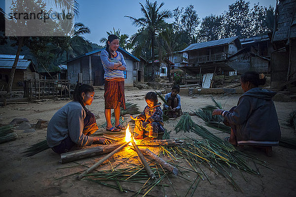 Frauen und Kinder wärmen sich an einem Feuer und verarbeiten Schilfrohr zur Herstellung von Besen in Ban Had Dan  Laos. Die mit Bambus umwickelten und zu Besen gefertigten Schilfbüschel werden ins benachbarte Vietnam verkauft und erzielen dort einen Preis von 3.000 Kip (0 37 $) - ein Heimgewerbe in diesem Dorf. Das Dorf würde durch den geplanten Staudamm Nr. 3 (mit dessen Bau noch nicht begonnen wurde) nur teilweise überschwemmt werden.