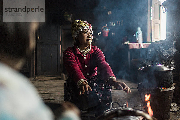 Junge Frau hockt vor einem Lagerfeuer und wärmt sich die Hände  Myanmar  Shan  Myanmar