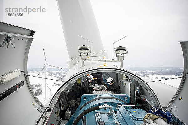 Zwei Wartungsarbeiter arbeiten im Winter an einer Windkraftanlage in Nordpolen bei Kobylnica: Dieses Foto von Experten bei der Arbeit zeigt eine ungewöhnliche Perspektive auf Windturbinen und wird wahrscheinlich als glaubwürdig und authentisch angesehen