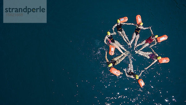 Luftaufnahme von jungen Mädchen  die schwimmen und ein Rad an der Oberfläche des tiefblauen Wassers bilden und ihre orangefarbenen Rettungsbojen im ligurischen Meer in der Nähe von Paraggi  Italien  aufhängen