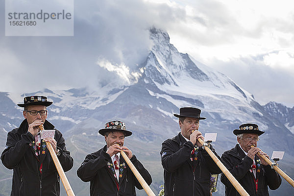 Vier traditionell gekleidete Einheimische aus Zermatt spielen vor dem Matterhorn auf dem Alphorn. Im Laufe der Zeit verschwand das Alphorn als Instrument der Schweizer Hirten fast vollständig. Erst mit der Romantik des 19. Jahrhunderts und der Wiederbelebung von Folklore und Tourismus erlebte das Alphorn eine Renaissance und wurde sogar zu einem nationalen Symbol.