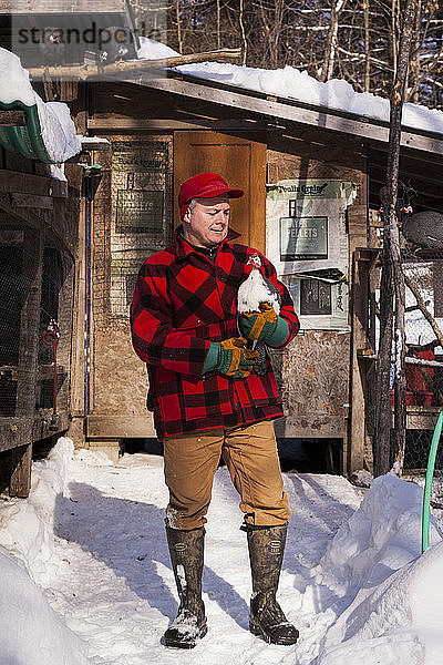 Porträt eines Bauern  der an einem Wintertag vor einem Hühnerstall liebevoll ein Perlhuhn betrachtet.