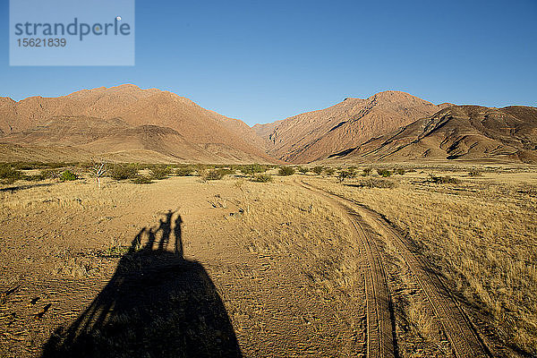 Foto mit Schatten von vier Personen auf einem Hügel und Landschaft mit Hügeln  Brandberg  Damaraland  Namibia