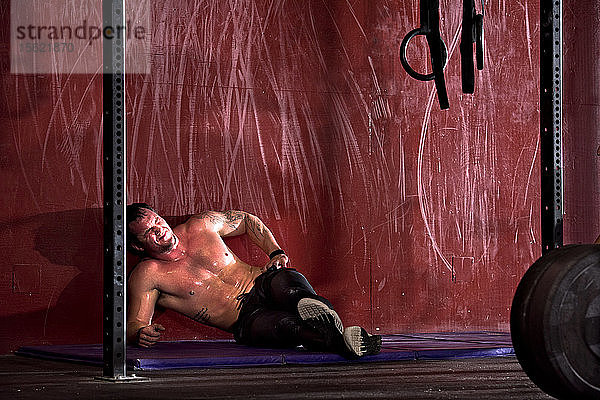 Ein Sportler sitzt nach einem intensiven Training in einem Fitnessstudio in San Diego  Kalifornien  mit Schmerzen auf dem Boden.