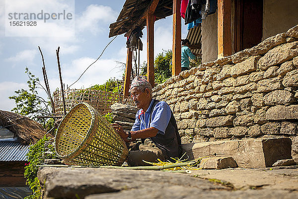 Ein alter nepalesischer Mann webt einen Korb vor seinem Haus in einem kleinen Dorf  Nepal