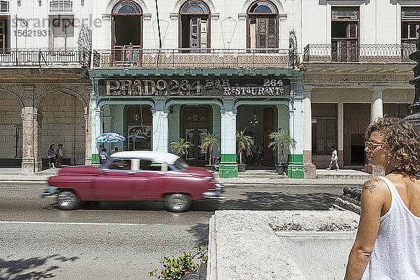 Touristisches Mädchen in den Straßen von La Habana mit einem alten Auto  das sich im Hintergrund bewegt