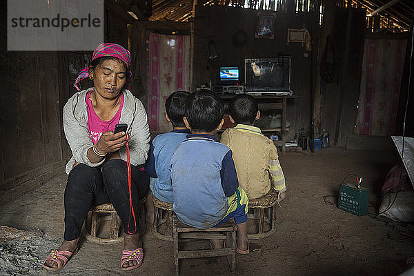 Eine Mutter spielt Musik von ihrem Handy ab  während ihr Sohn und zwei seiner Freunde zu Hause in Ban Sop Kha  Laos  fernsehen. Die elektronischen Geräte werden mit Batterien (rechts) betrieben  die von Kleinstwasserturbinen geladen werden  die in den Nam Ou-Fluss eingebaut wurden.