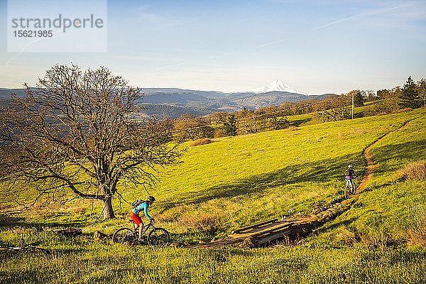 Eine junge Frau fährt mit dem Mountainbike auf einem einspurigen Weg durch grünes Gras in der frühen Morgensonne.