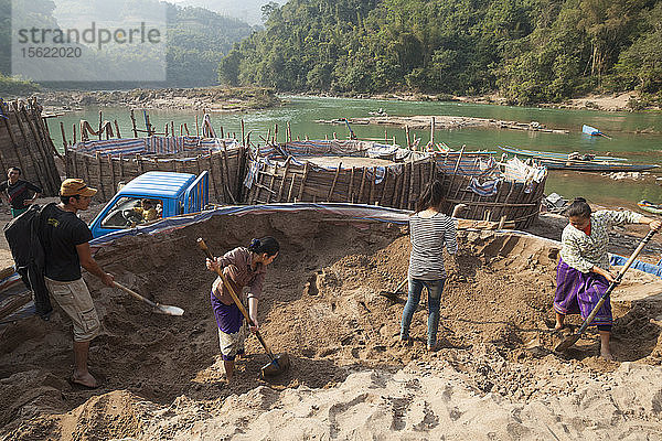 Loa-Männer und -Frauen  die für SinoHydro arbeiten  schaufeln Sand am Ufer des Nam Ou-Flusses in Hat Sa  Laos. Der Sand wird zur Herstellung von Beton für den Bau des Staudamms Nr. 6 flussaufwärts verwendet.