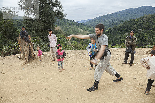 Robert Hahn versucht (erfolglos)  unter Anleitung der Kinder in Ban Sop Kha  Laos  einen Holzkreisel zu werfen.