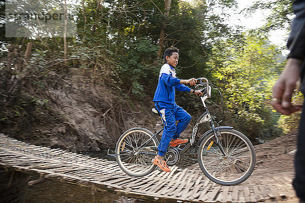 Ein Junge fährt mit seinem Fahrrad über die geflochtene Bambusbrücke über den Nebenfluss des Nam Ou außerhalb von Ban Huay Phouk  Laos.