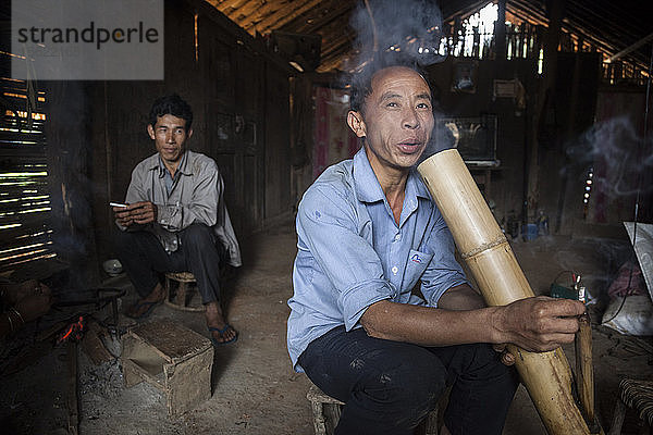 Ein Mann raucht in seinem Haus in Ban Sop Kha  Laos  eine Zigarette durch eine große Wasserpfeife aus Bambus. Er erklärt  dass das Rauchen von Zigaretten auf diese Weise besser für seine Lunge sei.
