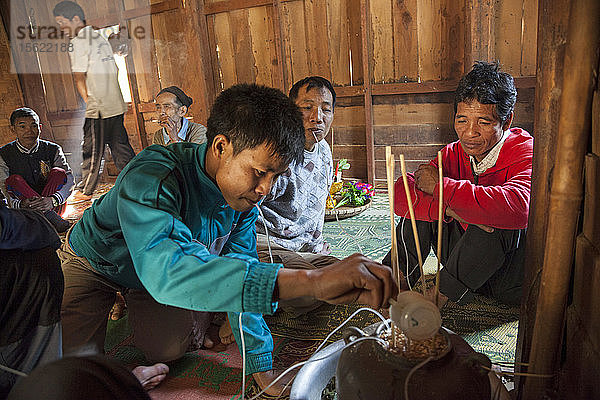 Männer trinken Lao Hai (Reiswein in Tonkrügen) aus langen Strohhalmen bei einer Glücksfeier im Haus einer krebskranken Frau in Ban Huay Phouk  Laos.