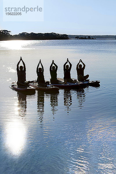 Foto mit Silhouette einer Gruppe von Menschen  die Yoga auf Paddelbrettern machen