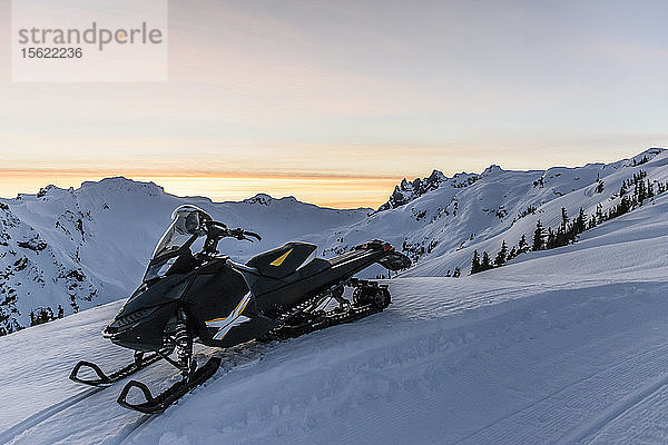 Einzelnes Schneemobil auf einem Berg im Winter unter stimmungsvollem Himmel bei Sonnenuntergang  Callaghan Valley  Whistler  British Columbia  Kanada
