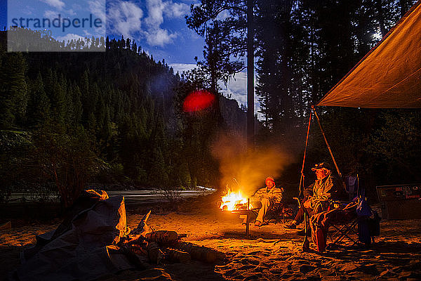 Blick auf zwei Männer auf einem Campingplatz mit Lagerfeuer bei Sonnenuntergang in der Nähe des Salmon River  Idaho  USA