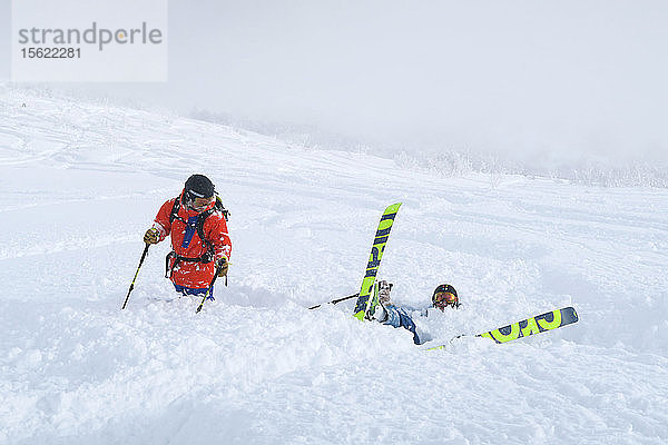 Eine Freeriderin stürzt in den Tiefschnee  ihr Freund schaut zu. Der Schnee im Skigebiet Niseko United auf der japanischen Insel Hokkaido ist so weich  dass es beim Sturz absolut nicht weh tut. Die Skier  die das Paar benutzt  sind groß und breit  so dass die Wintersportler die hüfttiefen Tiefschneehänge  für die Niseko United bekannt ist  in vollen Zügen genießen können. Niseko United besteht aus vier Skigebieten auf einem Berg  dem Annupuri (1.308 m). Der 100 km südlich von Sapporo gelegene Niseko Annupuri ist ein Teil des Quasi-Nationalparks Niseko-Shakotan-Otaru Kaigan und der östlichste Park der Niseko-Vulkangruppe. Hokkaido  die nördliche Insel Japans  liegt geografisch ideal in der Bahn der beständigen Wettersysteme  die die kalte Luft aus Sibirien über das Japanische Meer bringen. Dies führt dazu  dass viele der Skigebiete mit Pulverschnee überhäuft werden  der für seine unglaubliche Trockenheit bekannt ist. In einigen der Skigebiete Hokkaidos fallen durchschnittlich 14-18 Meter Schnee pro Jahr. Niseko ist die Pulverschneehauptstadt der Welt und als solche das beliebteste internationale Skigebiet in Japan. Es bietet ein unvergessliches Erlebnis für Skifahrer und Snowboarder aller Niveaus.