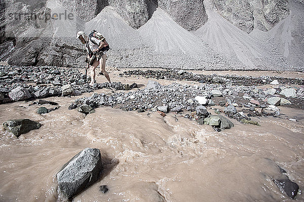 Ein Bergsteiger überquert einen Fluss auf dem Weg zum vorgeschobenen Basislager des Peak Lenin (Kirgisistan).