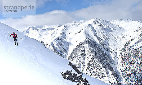 Ein Skifahrer fährt den Silverton Mountain mit anderen schneebedeckten Gipfeln im Hintergrund hinunter.