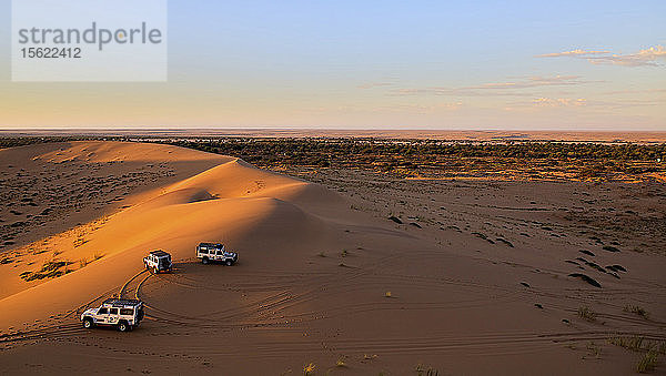 Drei Fahrzeuge  die in der untergehenden Sonne auf den Sanddünen geparkt sind