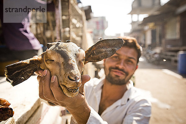 Ein Straßenhändler hält einen Ziegenkopf in Jaipur  Indien.