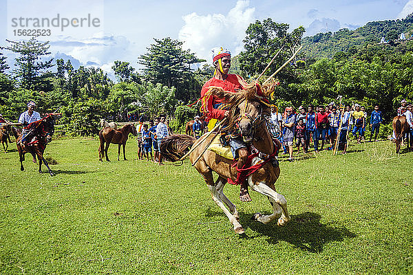Junger Mann in Tracht reitet auf einem Pferd und hält einen Speer beim Pasola-Festival  Insel Sumba  Indonesien