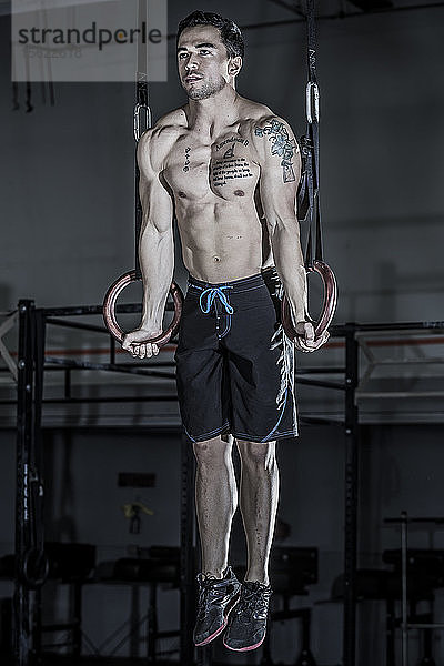 Ein männlicher Gewichtheber und CrossFit-Sportler ohne Hemd  der in einem CrossFit-Fitnessstudio einen Muskelaufschwung durchführt.