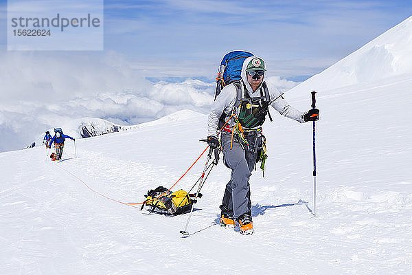 Skibergsteiger und Ranger auf dem Weg zu 14.000 Fuß auf dem Denali in Alaska. Bergsteiger auf dem höchsten Gipfel Nordamerikas tragen ihre Lasten in Rucksäcken und auf Schlitten.