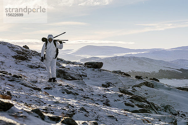 Ein Fotograf  der ein Stativ auf dem Rücken trägt und durch eine verschneite Landschaft läuft