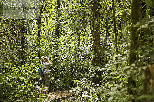 Ein männlicher Wanderer schaut durch ein Fernglas im Monteverde-Nebelwald  Costa Rica