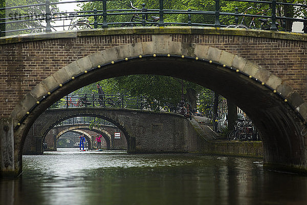 Zwei Personen auf einem Paddelboot im Stadtkanal unter Bogenbrücken  Amsterdam  Amsterdam  Niederlande