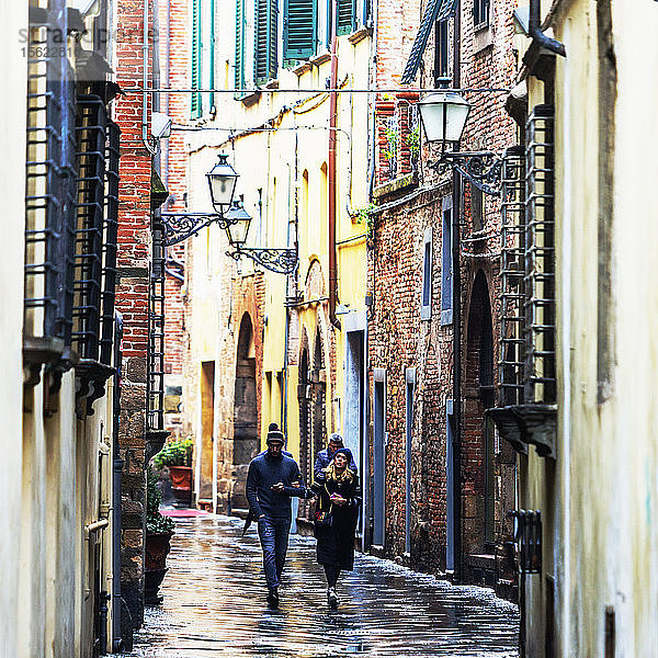 Frontansicht von Menschen  die durch die nassen Straßen der Stadt Lucca laufen  einer Stadt und Gemeinde in der Toskana  Mittelitalien  am Serchio  einer fruchtbaren Ebene in der Nähe des Tyrrhenischen Meeres. Sie ist die Hauptstadt der Provinz Lucca. Sie ist berühmt für ihre intakten Stadtmauern aus der Renaissancezeit.