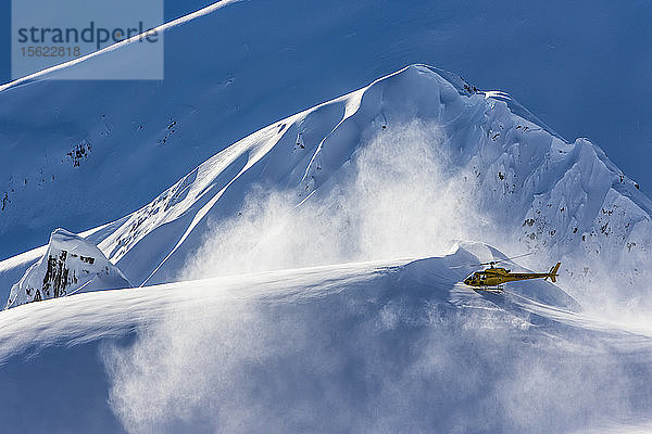 Ein Hubschrauber  der Skifahrer und Snowboarder auf die Gipfel der Berge bringt  hebt ab und bläst an einem sonnigen Tag in Haines  Alaska  Schnee in die Luft.