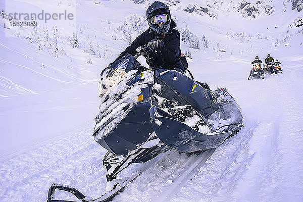 Abenteuerlustiger Mann schaut in die Kamera  während er im Callaghan Valley  Whistler  British Columbia  Kanada  Schneemobil fährt