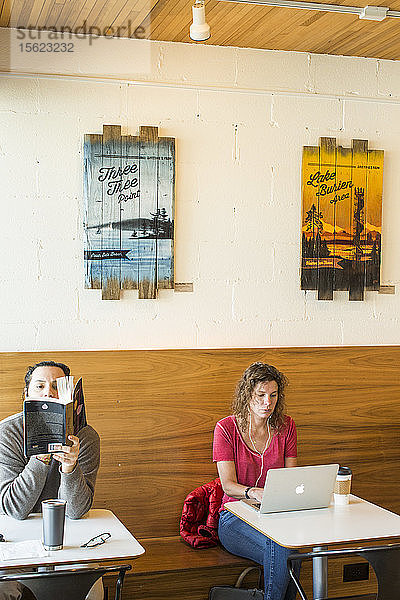 Ein Mann liest ein Buch in einem Café neben einer Frau  die auf einem Laptop tippt  Seattle  Washington  USA