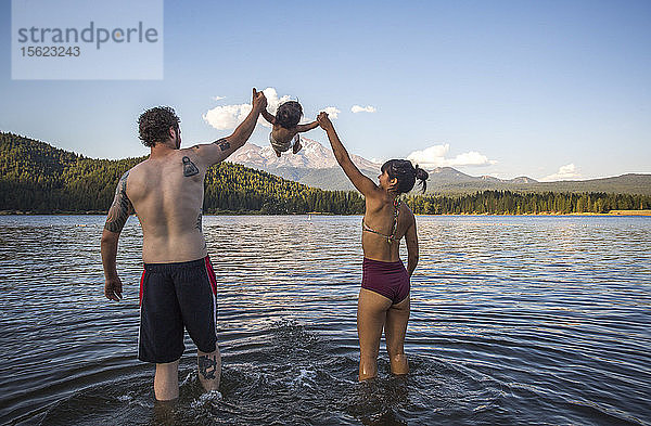 Rückansicht eines Paares in Badeanzügen  das mit seiner kleinen Tochter im Lake Siskiyou  Kalifornien  USA  spielt