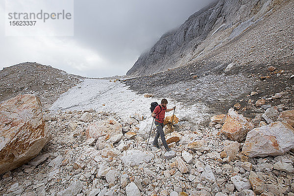 Ein Wanderer  der an einem kleinen Gletscherfeld in der mondähnlichen Landschaft des Gipfelplateaus auf dem Triglav  dem höchsten Berg Sloweniens  vorbeigeht