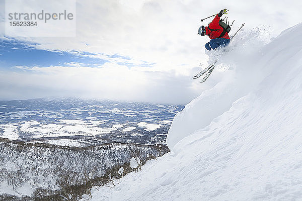 Ein männlicher Skifahrer springt auf einer Tiefschneepiste im Skigebiet Niseko United auf der japanischen Insel Hokkaido in die Luft.