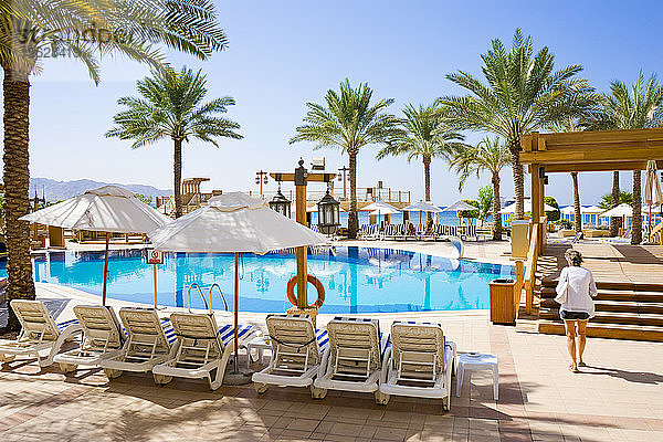 Frau  die am Pool in einer Ferienanlage mit Palmen spazieren geht  Aqaba  Jordanien