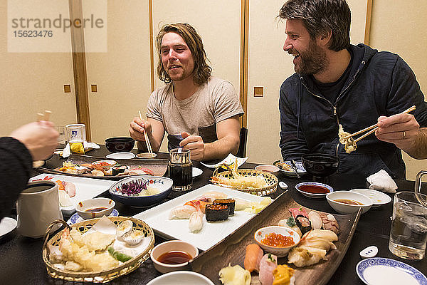 Ein europäischer Mann macht das Wasabi-Gesicht  während er in der Hafenstadt Otaru  Hokkaido Japan  Sushi isst  während seine Freunde lachen.