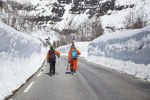 Zwei Skifahrer gehen auf einer Straße zwischen zwei hohen Schneewänden in der Nähe des Skigebiets Myrkdalen  Fjord  Norwegen