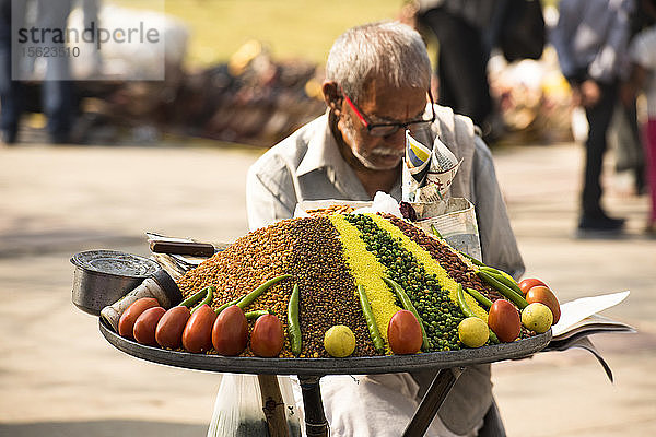 Ein indischer Mann liest die Zeitung  während er darauf wartet  dass die Leute sein buntes Essen kaufen.