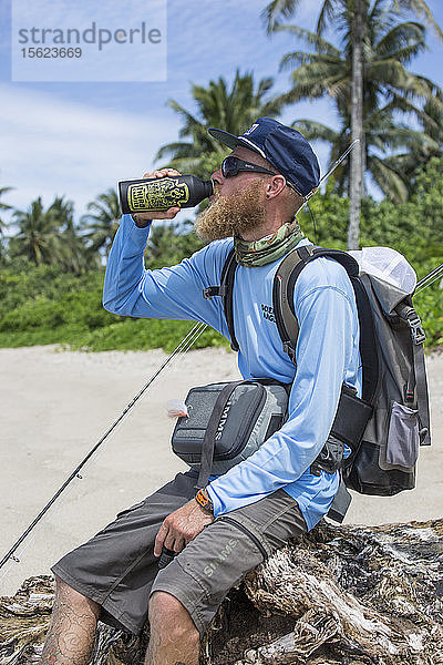 Der Angler Jonathan Jones trinkt aus einer Wasserflasche  während er an den Stränden Samoas auf der Suche nach Fliegenfischgewässern wandert.