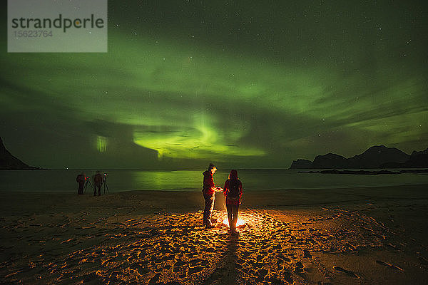 Ruhige Szene mit Menschen am Lagerfeuer am Strand unter Polarlicht  Flakstadoya  Lofoten  Norwegen  bei Nacht