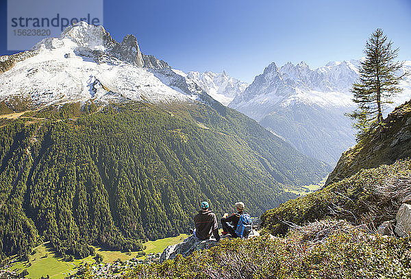 Zwei Wanderer genießen die Aussicht auf das Mont-Blanc-Gebirge  während sie eine Pause auf der Tour du Mont Blanc einlegen. Sie sind auf dem Weg zum Lac Blanc  oberhalb des Tals von Chamonix.