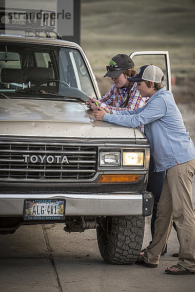 Zwei Mädchen schreiben eine SMS  während sie an einer Tankstelle in Montana mit einem Toyota Land Cruiser von 1990 tanken.